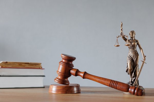 Die drei Symbole für Rechtsprechung - Gesetzesbücher, ein Richterhammer und die Statue der Justitia - stehen auf einem Tisch.