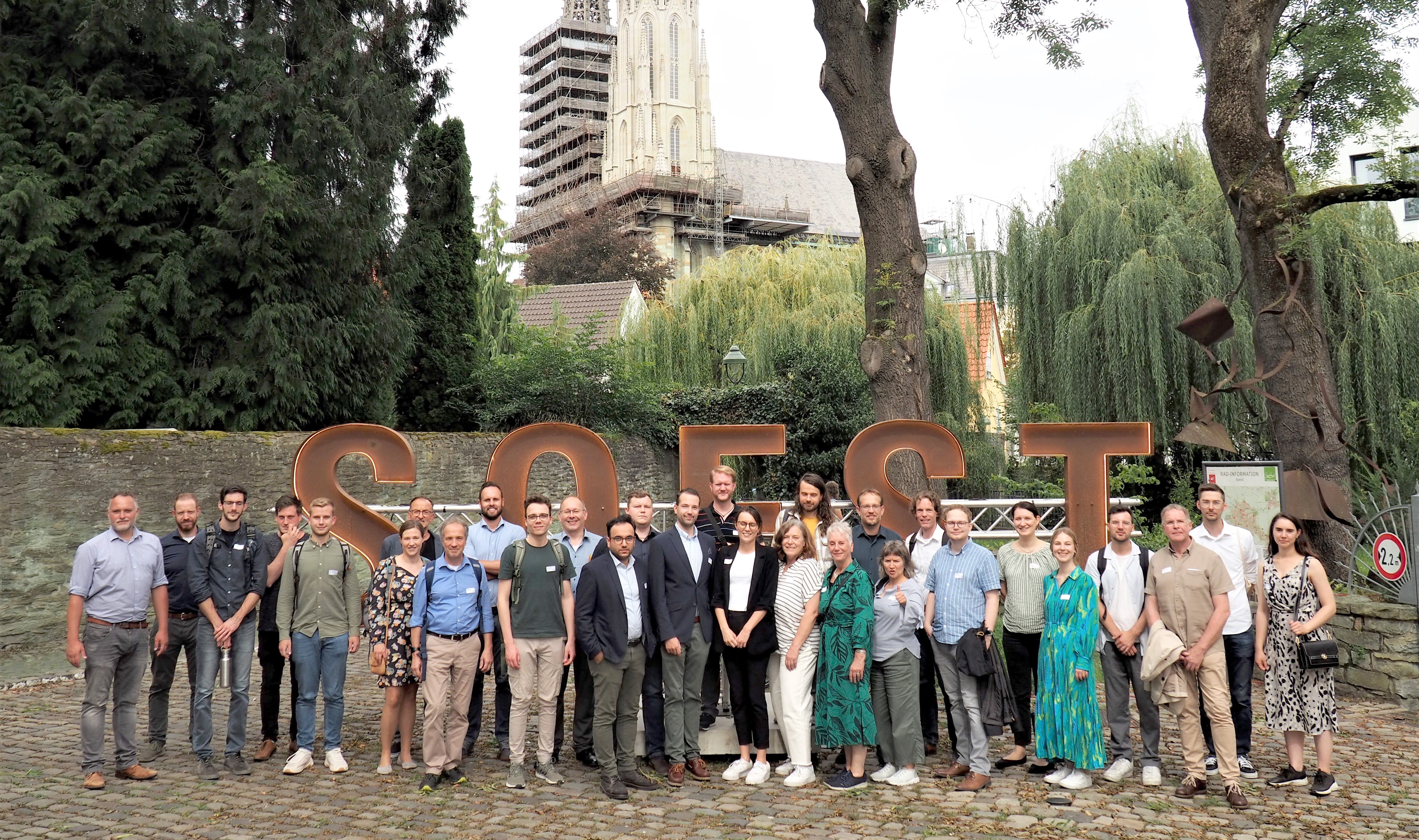 Das beiliegende Foto zeigt Gastgeber und Gäste bei dem Stadtrundgang vor dem Soest-Schriftzug an der Teichsmühle mit der Wiesenkirche im Hintergrund. 