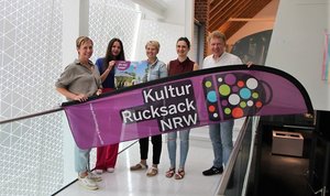 Elke Schmücker (Stadt Soest), Swetlana Ritter (Stadt Geseke), Sabrina Janetzky (Stadt Lippstadt), Jeanette Metz (Bad Sassendorf) und Uwe Albert (Stadt Lippstadt). präsentieren auf einer Treppe stehend das Banner der Reihe Kulturrucksack.