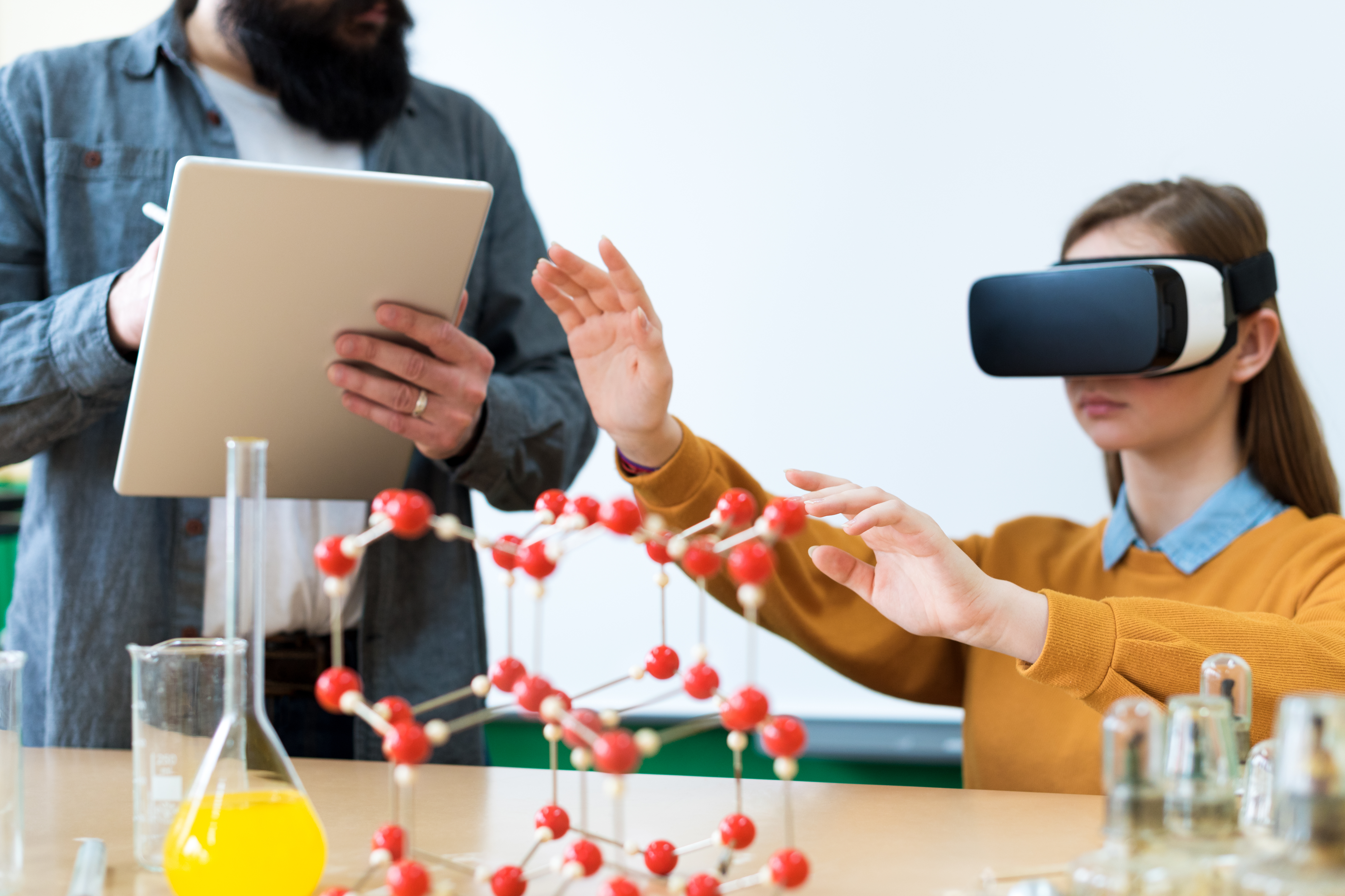 Young teacher using Virtual Reality Glasses and 3D presentation to teach students in chemistry class. Education, VR, Tutoring, New Technologies and Teaching Methods concept.